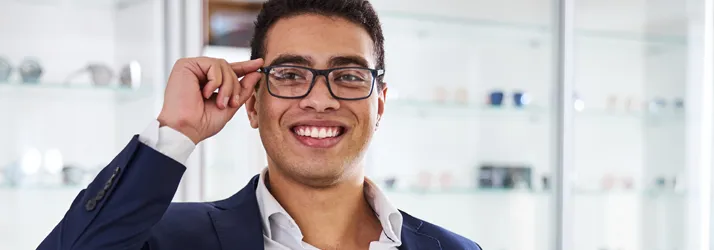 A man standing in an optometry office after getting his eyeglasses fitted. He adjusts them on his face.